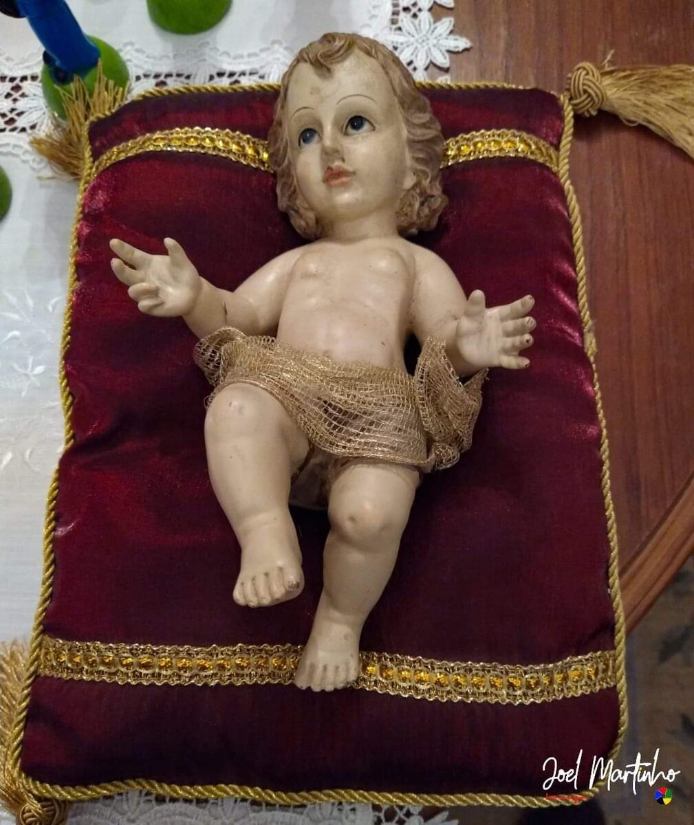 Menino Jesus deitado sobre almofada de cetim bordeaux com galão dourado