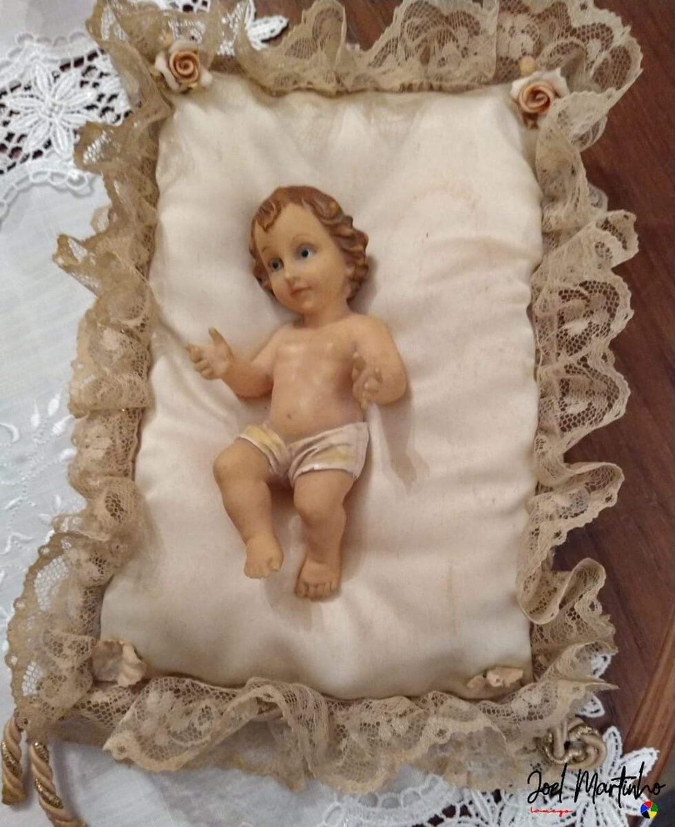 Menino Jesus sobre almofada de renda com rosas de porcelana nos cantos