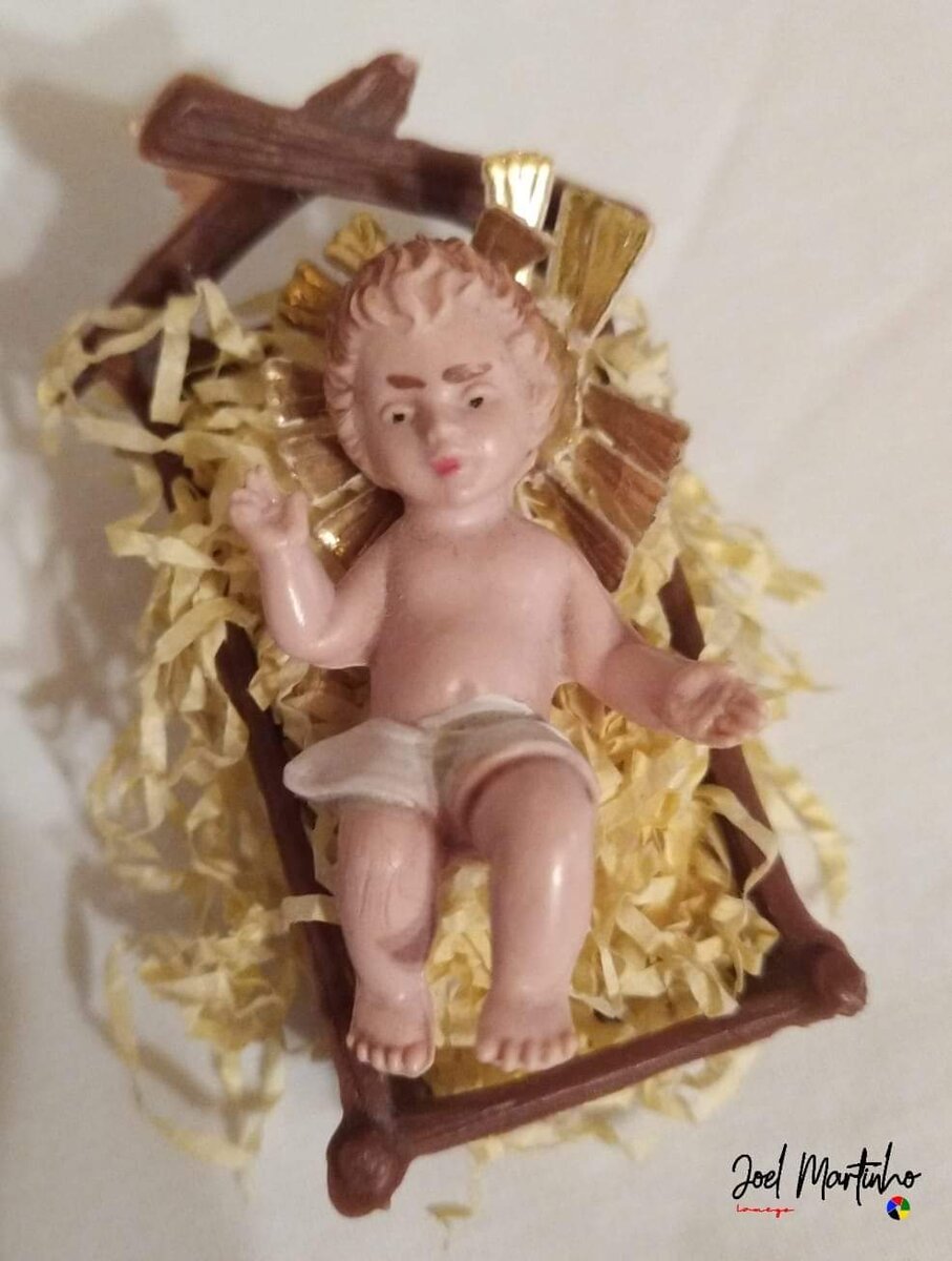 Menino Jesus em pequena manjedoura de madeira com palha e cruz ao fundo