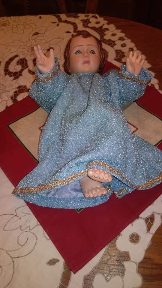 Menino Jesus deitado com túnica azul-prateada sobre coxim vermelho